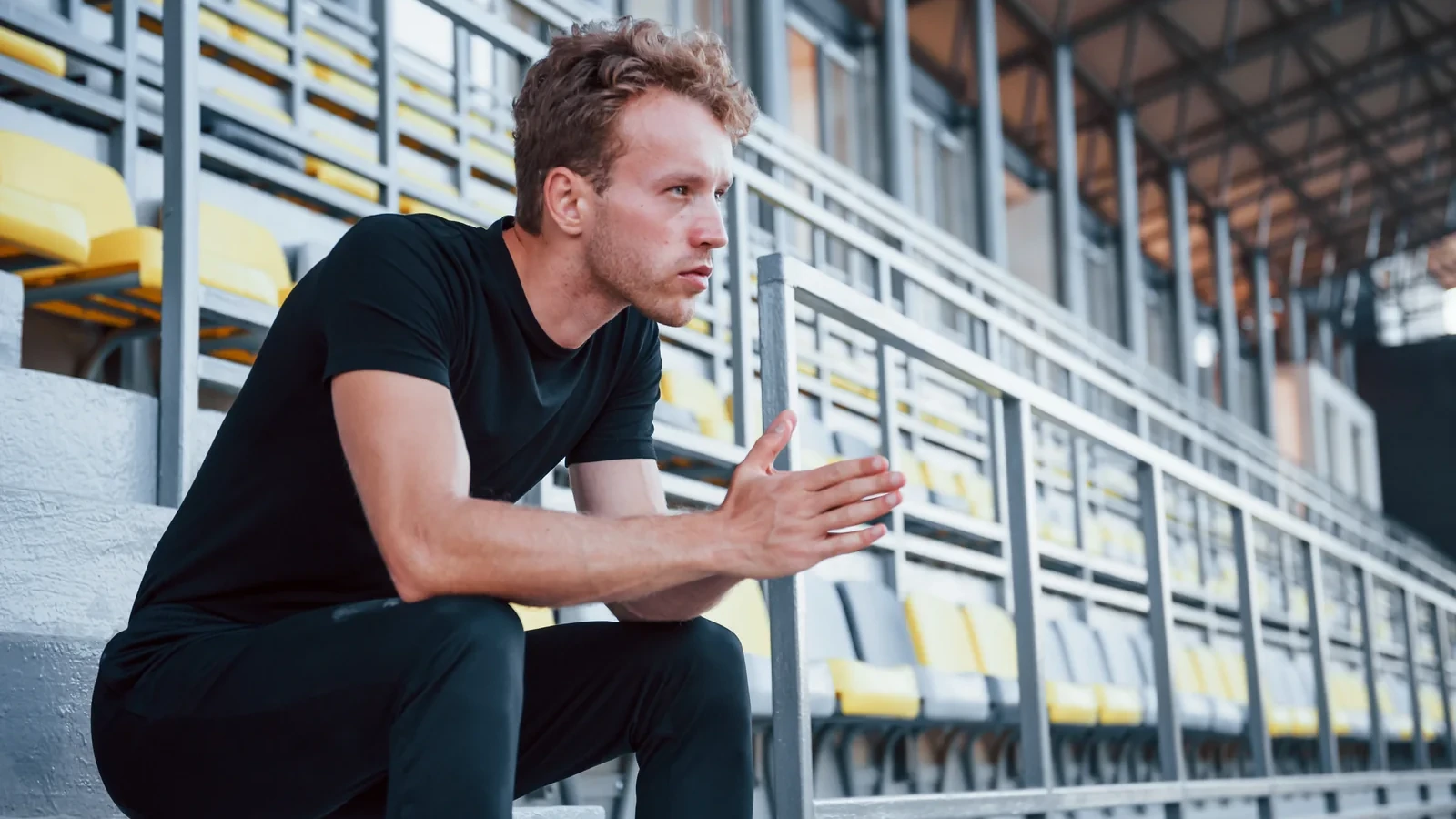 Coach sportif assis seul dans des tribunes, l'air épuisé