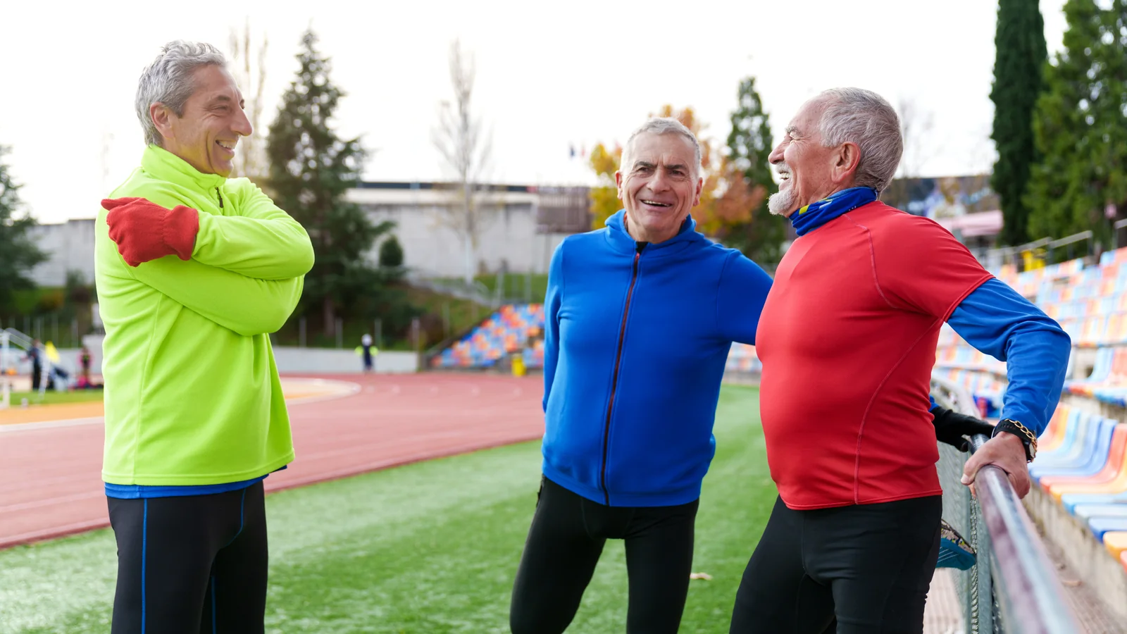 Trois seniors en tenue de sport discutant au bord d'une piste d'athlétisme avant une séance