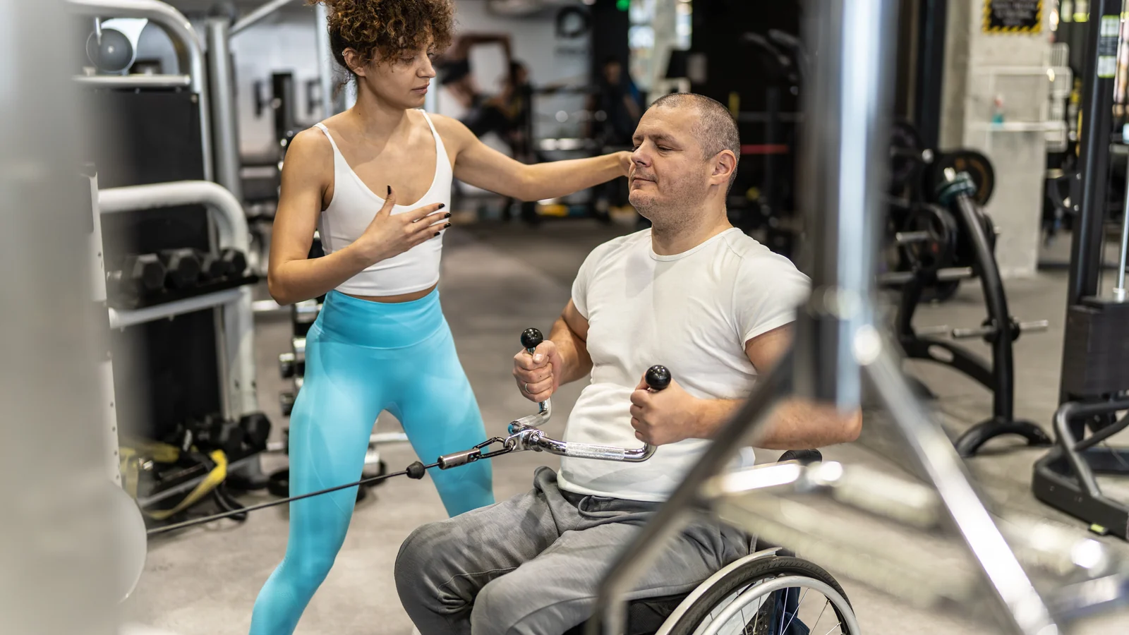 Coach sportive accompagnant un homme en fauteuil roulant sur une machine de musculation en salle