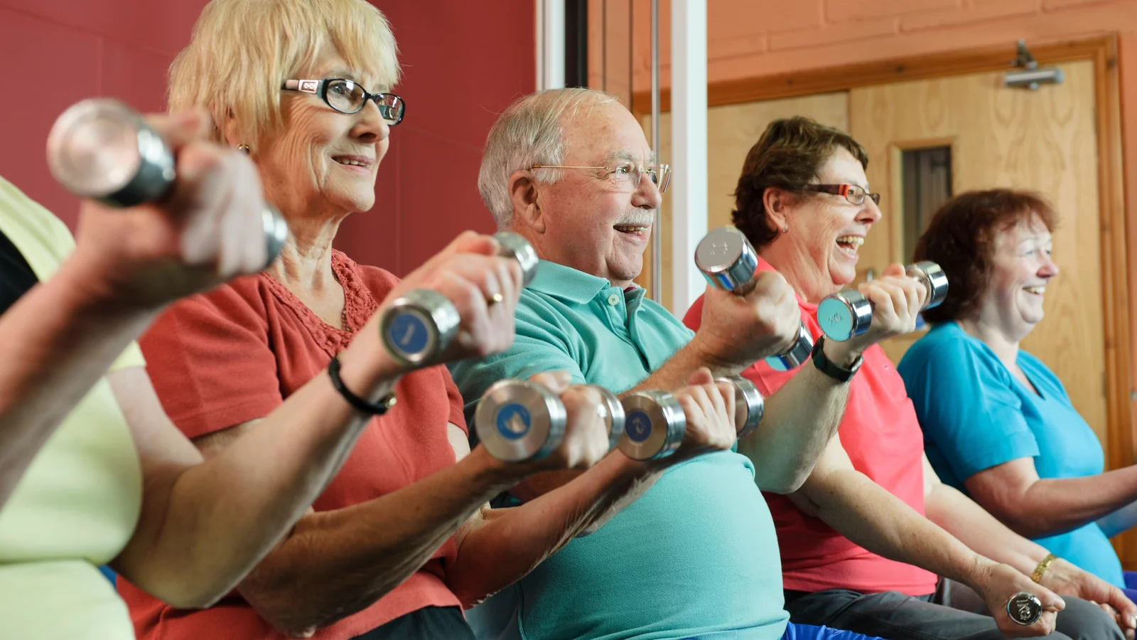 Groupe de seniors souriants réalisant un exercice avec haltères lors d'un cours collectif adapté