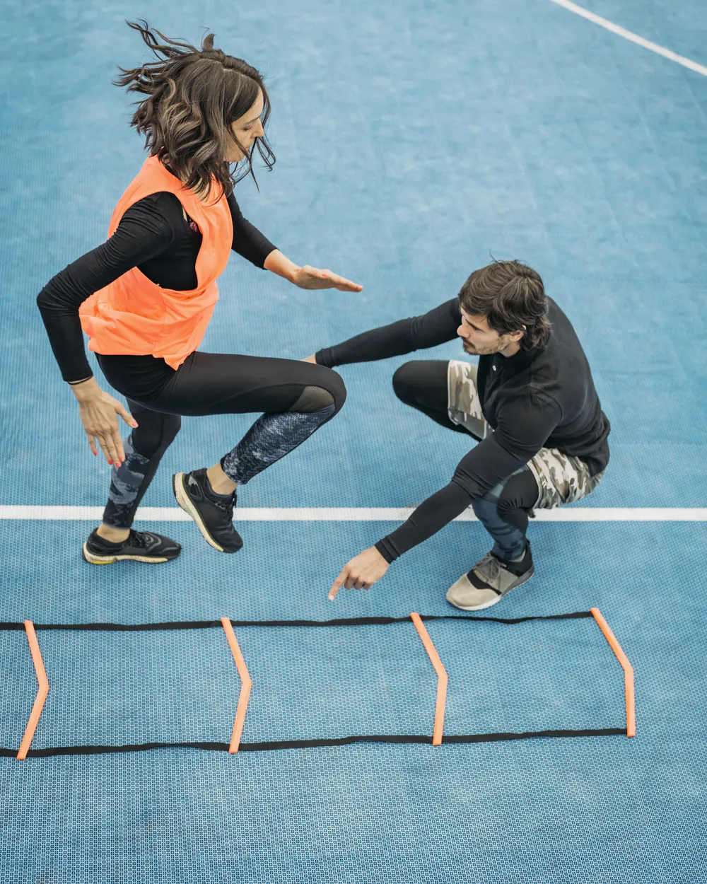 Sportive travaillant l'agilité sur une échelle de motricité, guidée par son coach